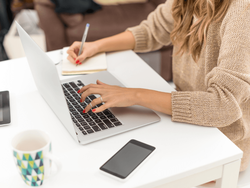 A marketing intern typing on a laptop and taking notes.