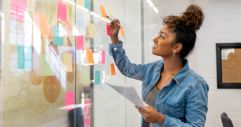 A woman brainstorming with post-it notes on a glass wall.