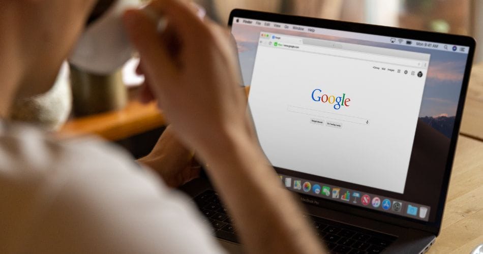 A person doing a google search on a laptop while drinking coffee