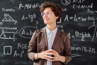 Female teacher in front of a blackboard with math equations written on it.